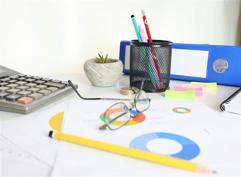 Mesa com calculadora, óculos, papéis e material de escritório organizados