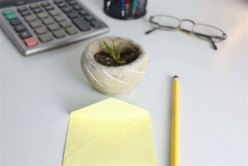 Mesa com calculadora, planta, óculos e um lápis