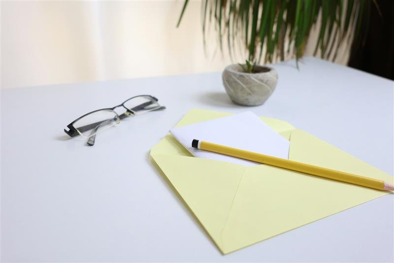Óculos, lápis e um bilhete sobre um envelope amarelo