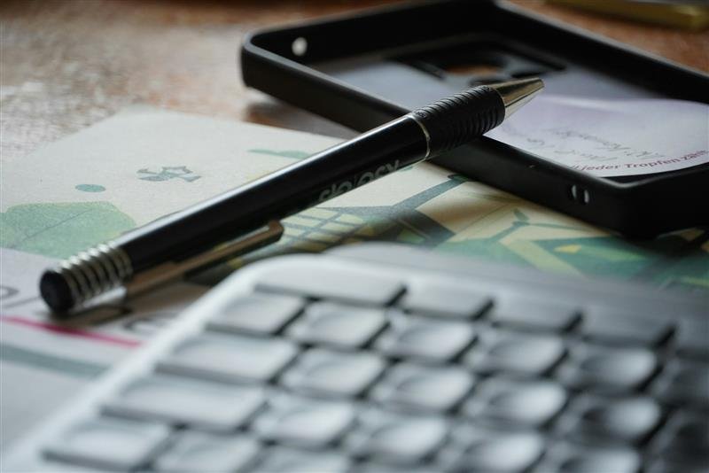 Celular, caneta e teclado sobre uma mesa de trabalho