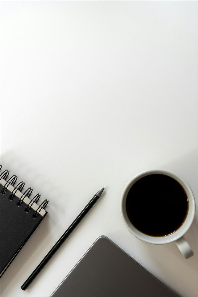 Notebook, caderno, lápis e xícara sobre mesa branca organizada