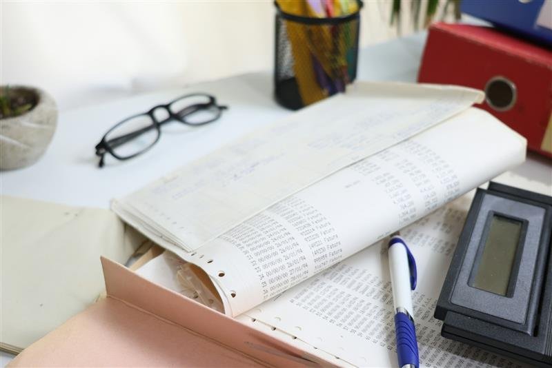 Mesa com papéis, óculos, calculadora e material de escritório