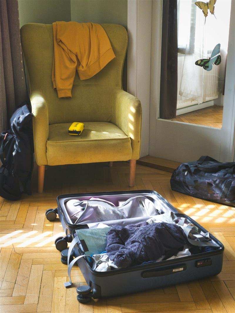 Mala aberta com roupas dentro, num quarto com poltrona